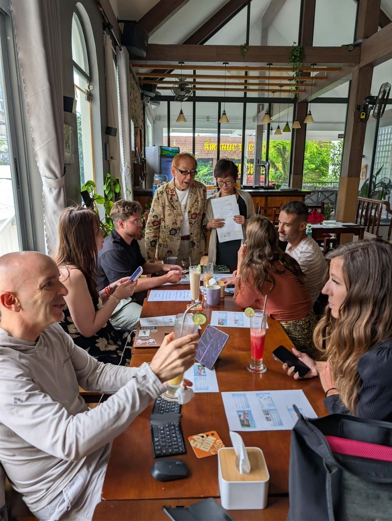 Mikiko and Hidehiko guiding international participants around a cafe table in Da Nang