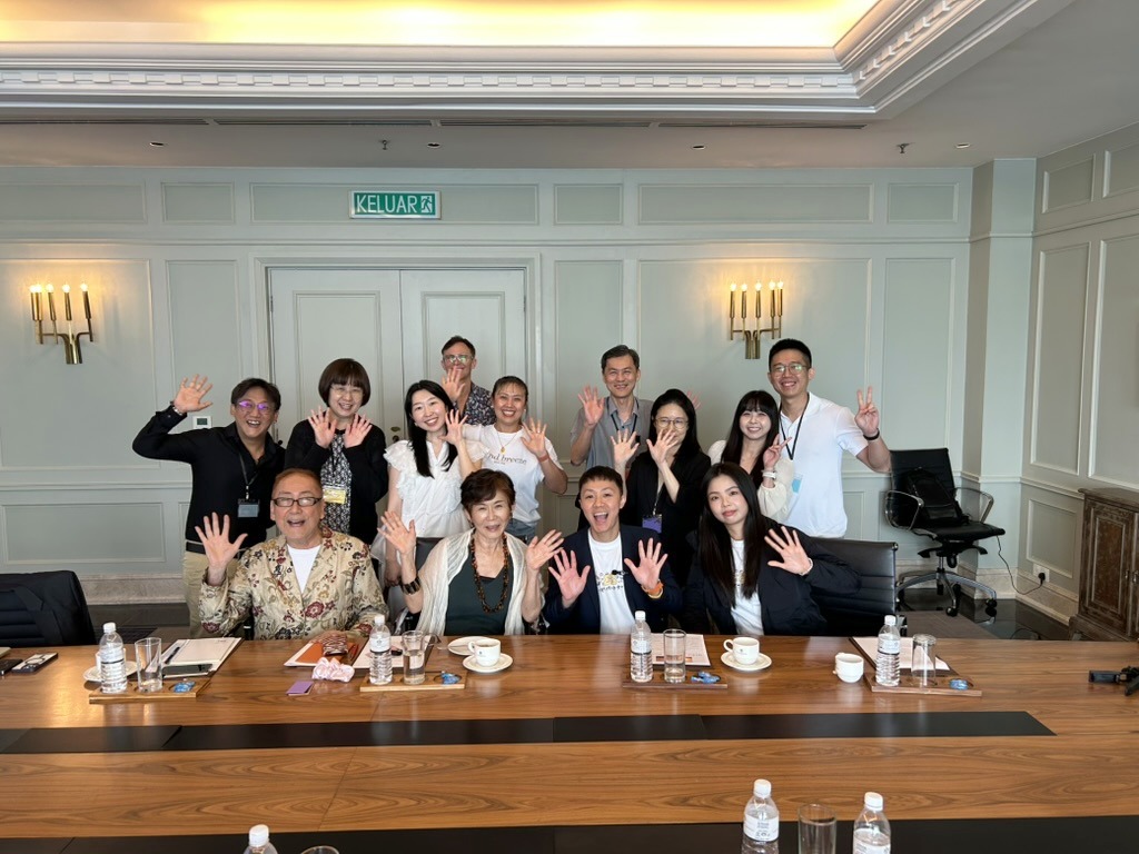 Retreat participants waving and smiling around a table in Penang