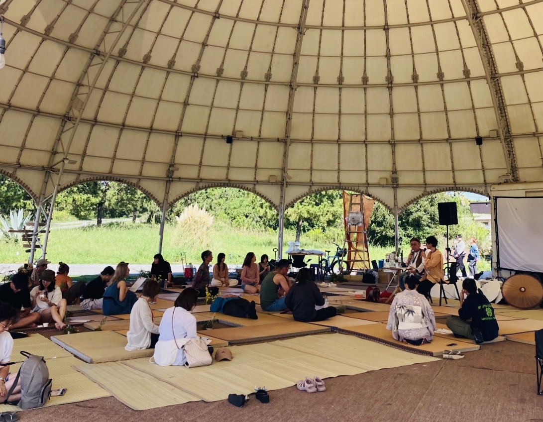 Participants seated on tatami mats in an open-air dome, listening to Mikiko and Hidehiko